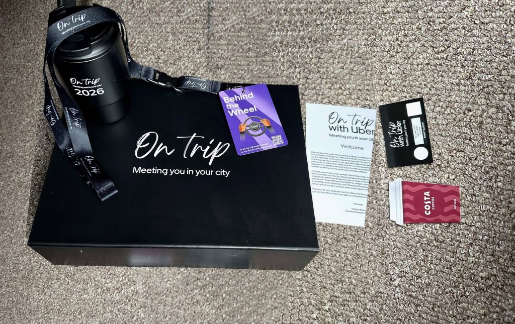 Uber "On Trip" driver listening session goodie box containing a branded mug, lanyard, Behind the Wheel podcast card, scratch card, Costa Coffee voucher, and welcome letter from Andrew Brem, General Manager Uber UK